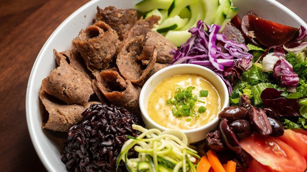 A plate with sliced meat, black rice, vegetables, and a dipping sauce. 2