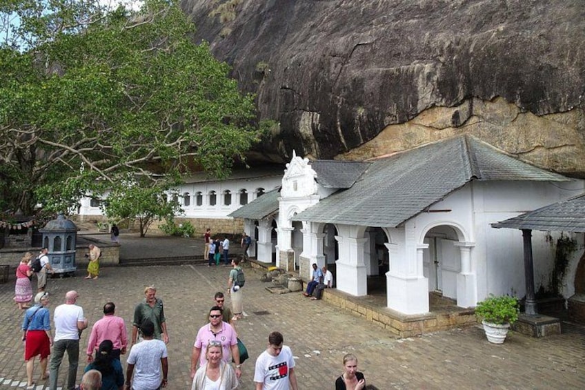 A white building with a tiled roof, surrounded by a paved area with people walking. 1