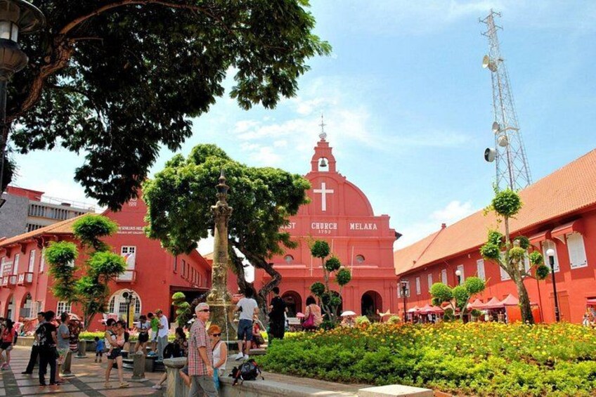 A red church with a cross, surrounded by people and greenery. 1