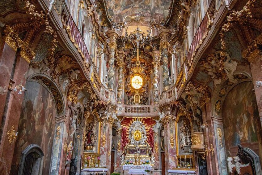 An ornate church interior with intricate gold decorations, a central chandelier, and a large altar. 1