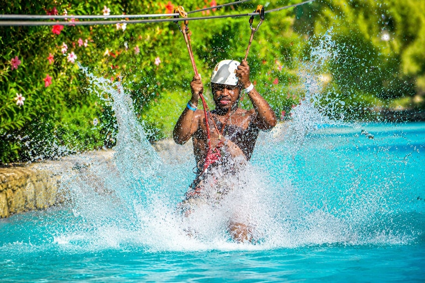 A person swinging over a pool, splashing water, with greenery and flowers in the background. 4