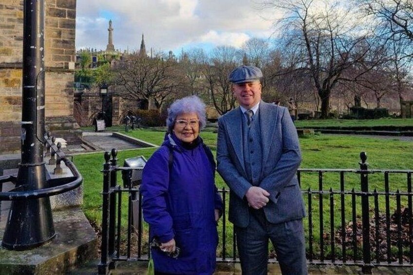Two people standing in a park with a fountain and a church in the background. 2