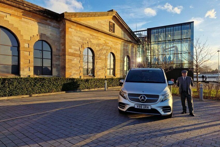 A silver Mercedes-Benz parked in front of a building with arched windows and a modern glass structure. 3