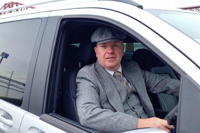 A person in a grey suit and hat sitting in a car. 4