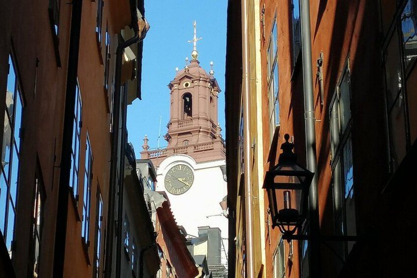 Une rue étroite bordée d’immeubles, avec un beffroi et un lampadaire. 3