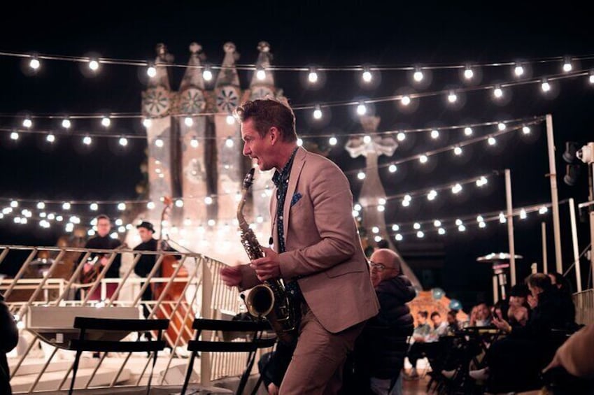 A person playing a saxophone on a stage with string lights and a clock tower in the background. 2
