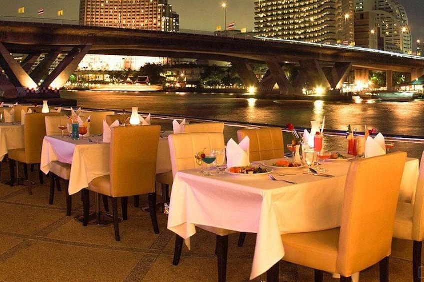 A waterfront restaurant with tables set for dining, a bridge in the background, and city buildings. 3