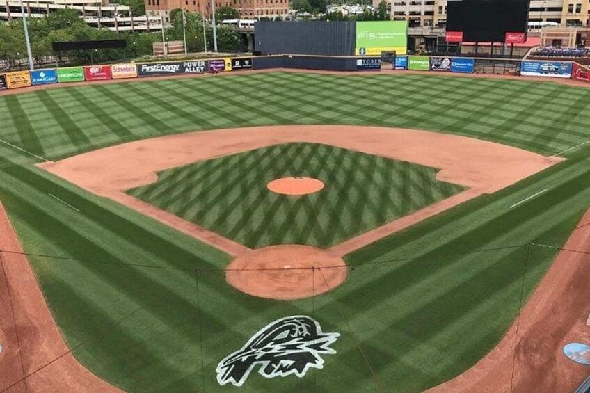 Un campo da baseball con un logo al piatto, pubblicità lungo il muro del fondo e un tabellone segnapunti sullo sfondo. 5