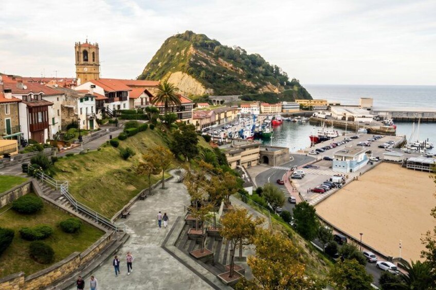 A coastal town with a prominent hill, a church, a marina with boats, and a sandy beach. 3