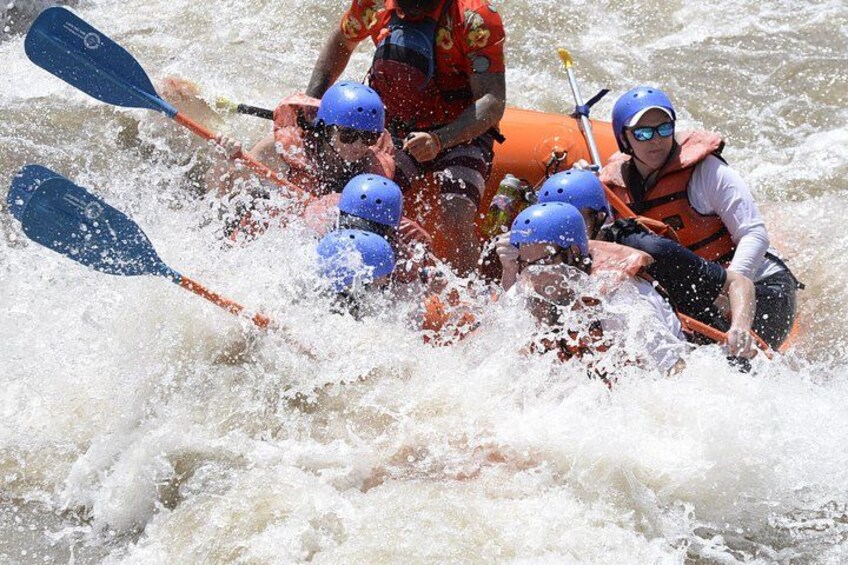 A group of people in an orange raft navigating through white water rapids. 2