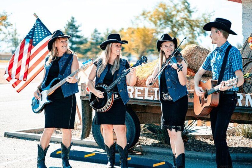 A group of musicians performing outdoors with an American flag and hay bales in the background. 3