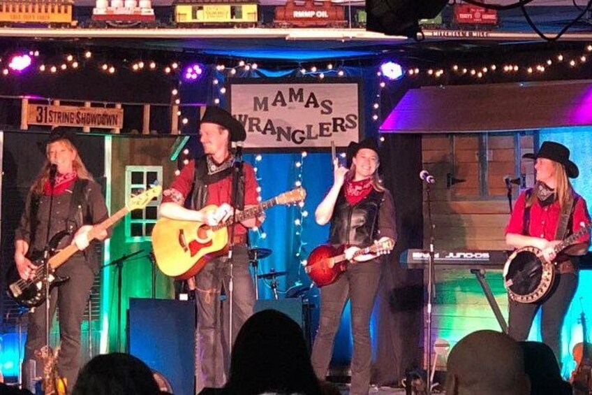 A band performing on stage with a sign reading "Mamas Ranchers". 2