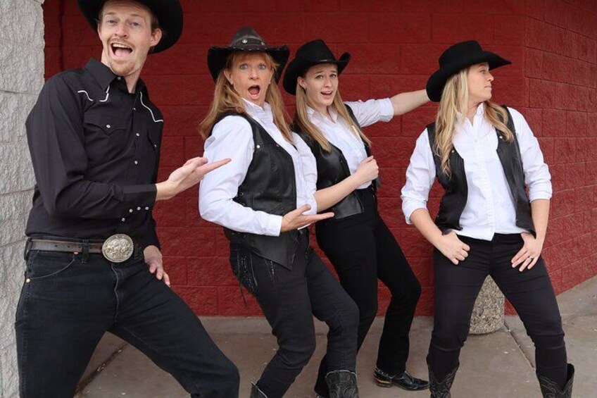 Four people in cowboy attire posing in front of a red wall. 4