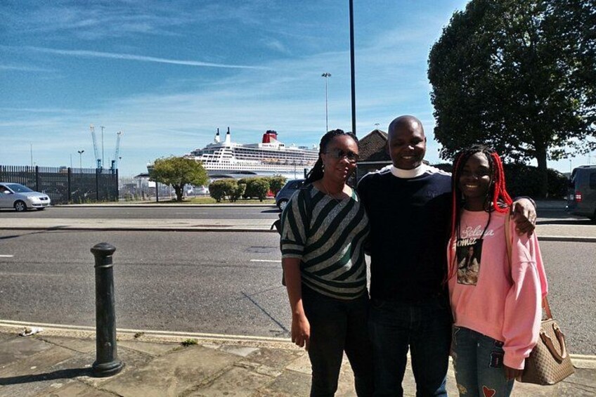 Three people standing on a sidewalk with a cruise ship in the background. 3