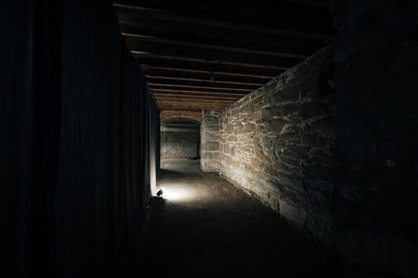 Un couloir de pierre faiblement éclairé, avec une seule source de lumière au bout. 2