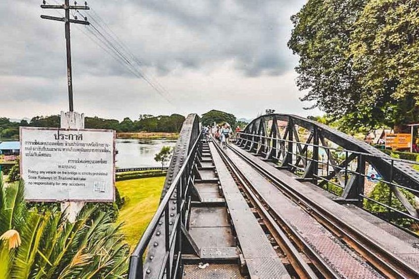 A railway bridge with a warning sign, tracks, and greenery. 3