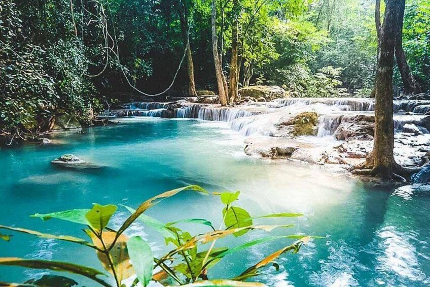 A clear blue river with a waterfall, surrounded by dense green foliage. 4