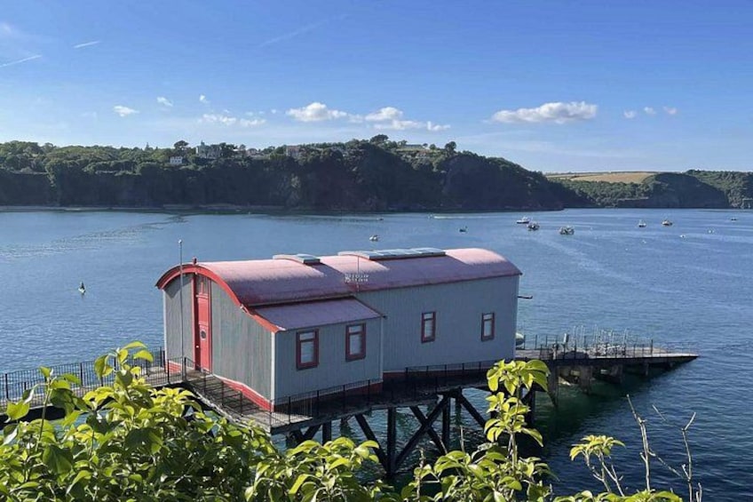 A houseboat on a calm lake with boats in the background and greenery on the shore. 3