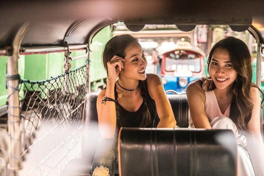 Two people sitting in a vehicle with a chain-link fence and a bus in the background. 3