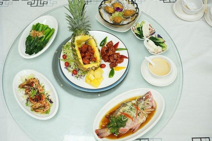 Un tavolo rotondo con diversi piatti, tra cui pesce, verdure e una composizione con ananas al centro. 4
