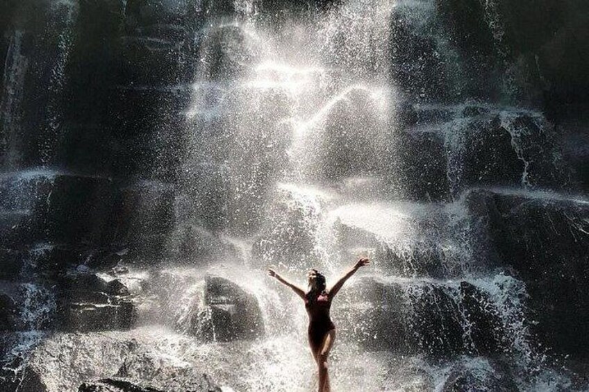 A person standing in front of a waterfall with arms raised. 2