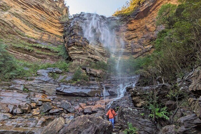 A waterfall cascading down a rocky cliff with a person standing at the base. 4