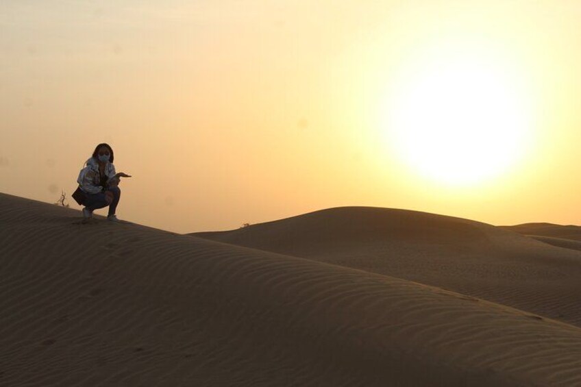 A person crouching on a sand dune with the sun setting in the background. 2