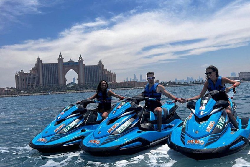 Three people jet skiing on a body of water with a large arch bridge in the background. 5