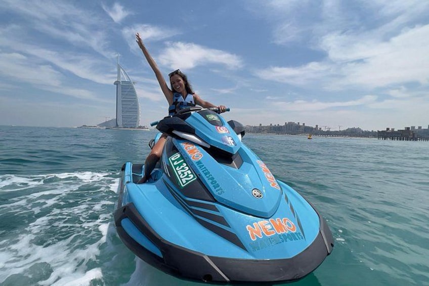 Una persona monta un jet ski azul sobre el agua, con un horizonte urbano y un edificio distintivo al fondo. 2