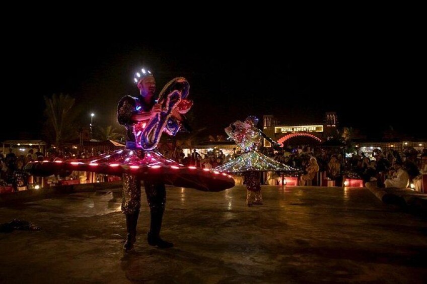 A nighttime outdoor event with performers in illuminated costumes, a crowd, and a building with a sign that reads 'Royal Adventure.' 2