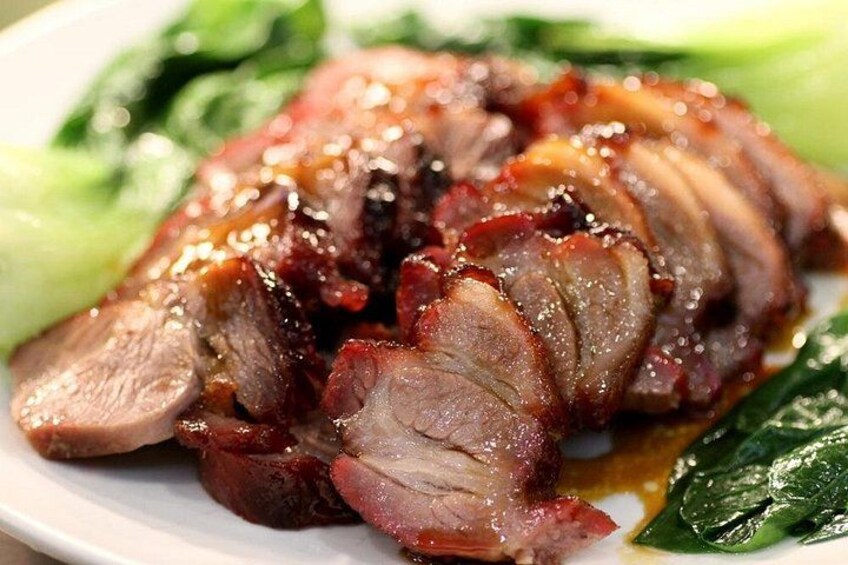 Sliced roasted duck with a glossy glaze, served on a white plate with green leafy vegetables. 1