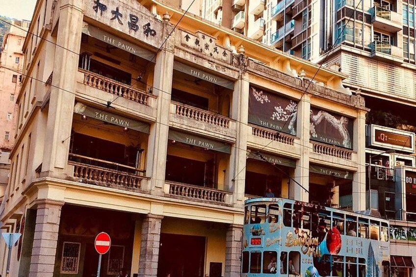 A multi-story building with balconies and signs reading 'The Pawn.' A blue double-decker bus is parked in front. 3