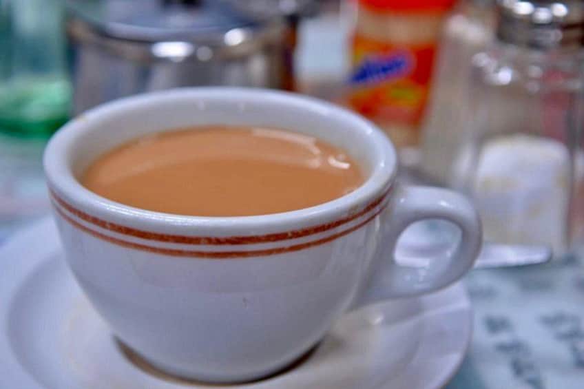 A white cup with a brown rim filled with a brown liquid, likely coffee, on a saucer. 4