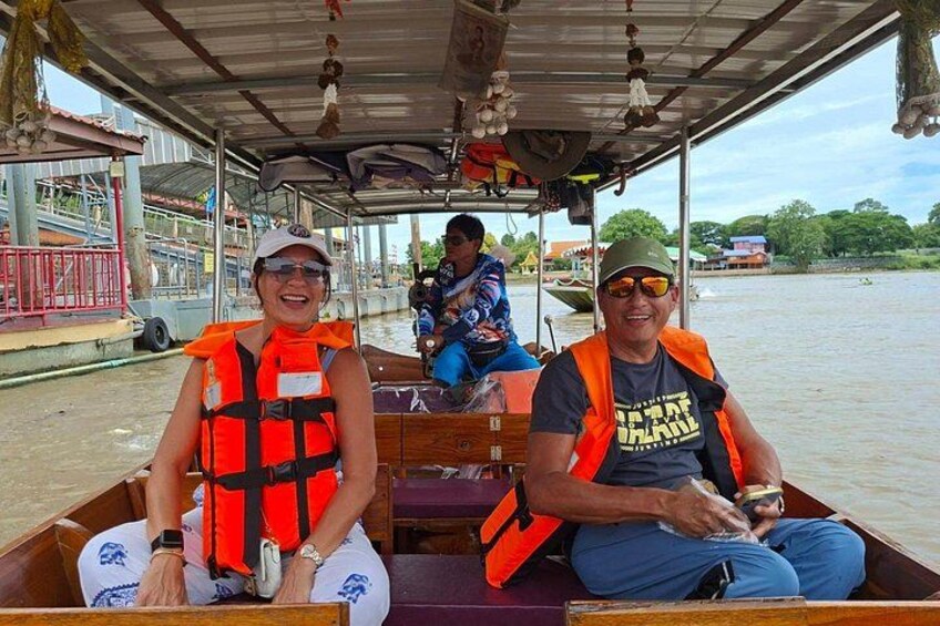 A boat with people wearing life jackets, a covered structure, and a river with buildings in the background. 4
