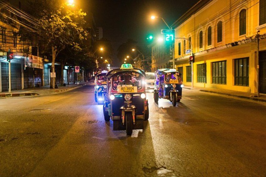 Een straatbeeld 's nachts met voertuigen, waaronder een taxi en tuk-tuks, en verlichte gebouwen. 4