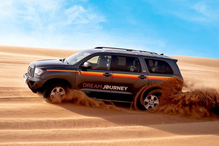 A black SUV with 'DREAM JOURNEY' on its side driving through a desert with sand dunes. 4