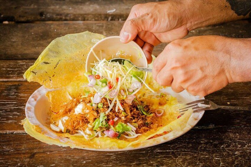 A person preparing a dish with a tortilla, shredded meat, and vegetables on a wooden table. 1