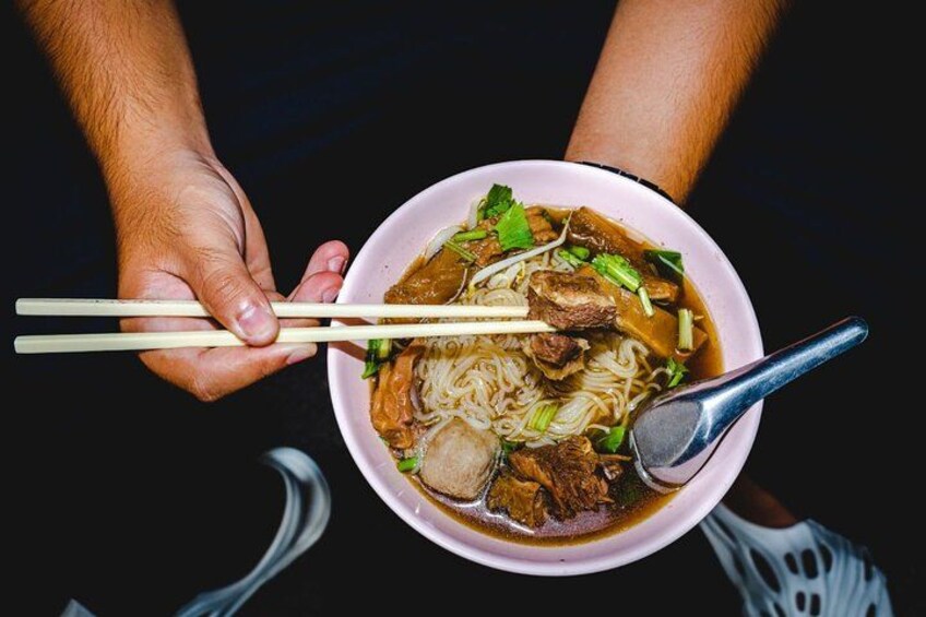 A bowl of noodle soup with chopsticks and a spoon. 5