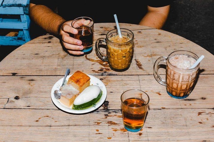 A wooden table with a plate of food, a glass of tea, and two drinks with straws. 2