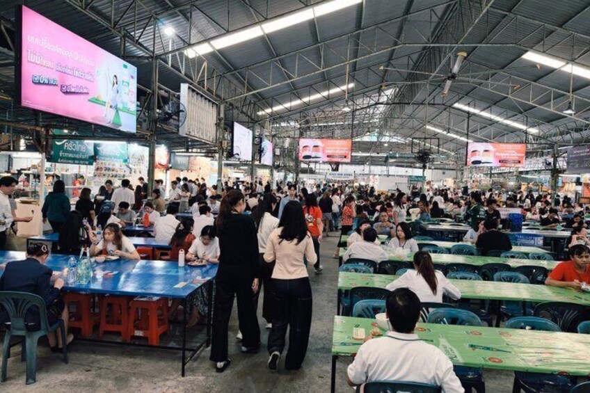 A crowded indoor market with people shopping and sitting at tables. 3