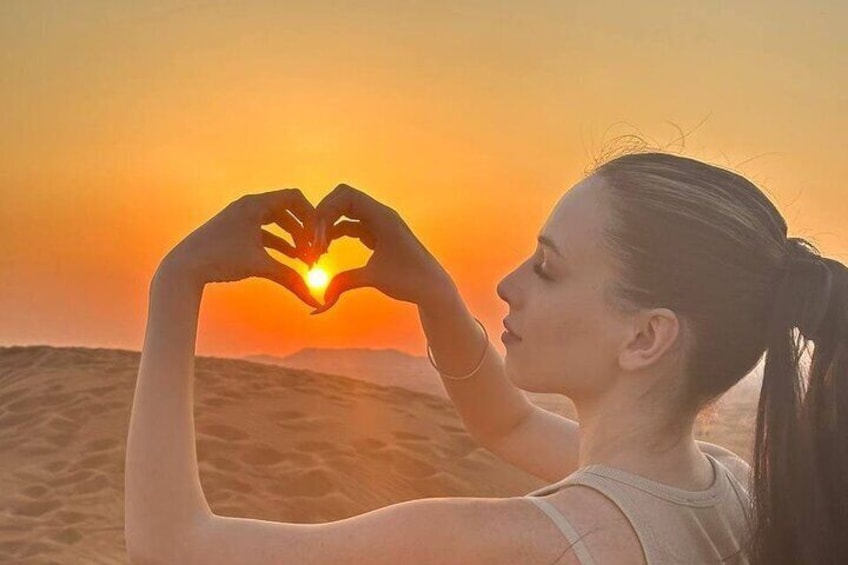 A person making a heart shape with their hands against a sunset. 1