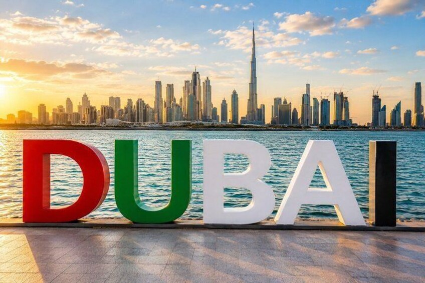 Le mot «
DUBAÏ
» est écrit en grandes lettres, dans les couleurs du drapeau des Émirats arabes unis, sur un fond représentant une vue panoramique de la ville et une étendue d’eau au coucher du soleil. 2