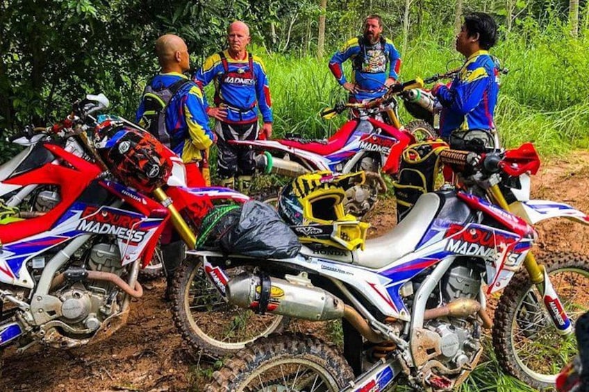 A group of dirt bikes parked on a dirt path surrounded by greenery. 5