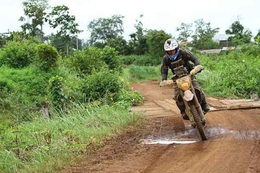 A person riding a dirt bike on a muddy trail surrounded by greenery. 4