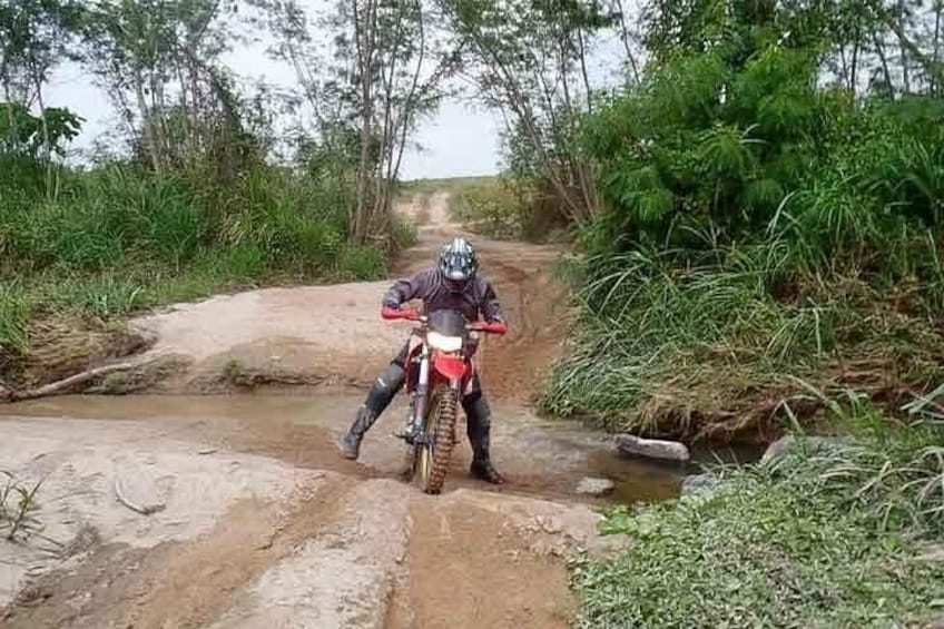 A person on a red dirt bike navigating a muddy trail with water crossings. 2