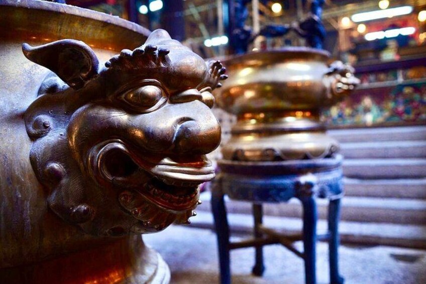 A bronze lion head sculpture and a golden incense burner in a temple setting. 3
