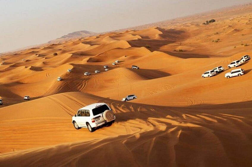 Un paysage désertique où l'on voit des véhicules blancs se déplacer à travers des dunes de sable. 4