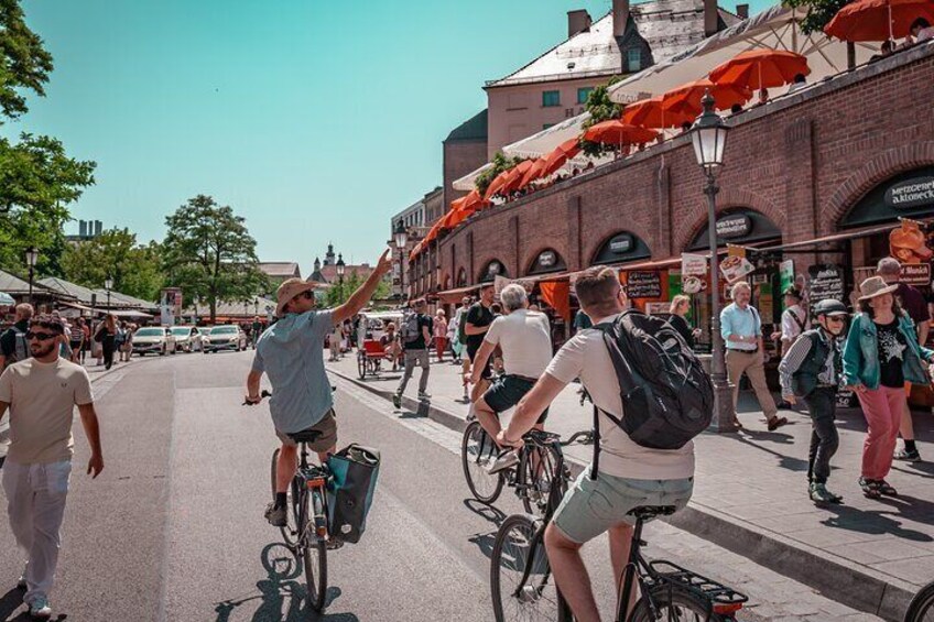 People walking and riding bicycles on a sunny street with brick buildings and orange umbrellas. 5
