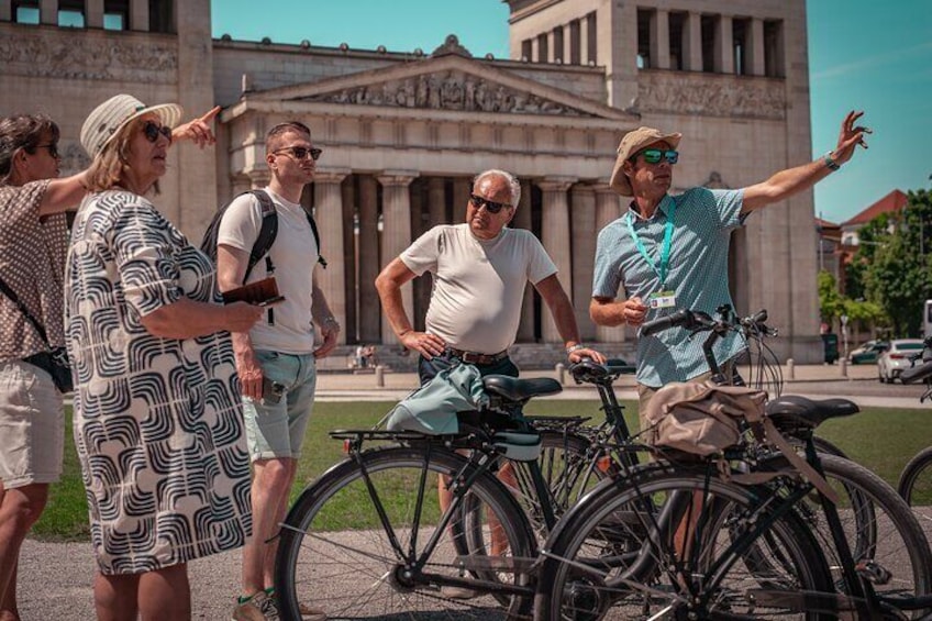 A group of people standing in front of a building with bicycles. 1