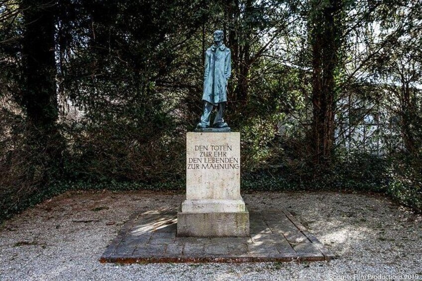A statue of a man on a pedestal with a plaque in a wooded area. 2